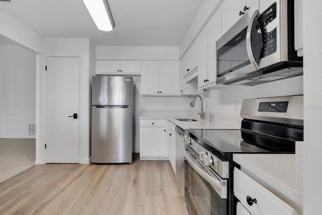 kitchen with light wood finished floors, stainless steel appliances, visible vents, white cabinetry, and a sink