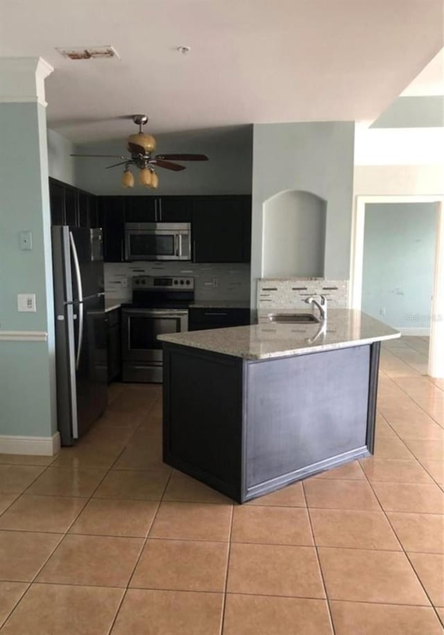 kitchen with appliances with stainless steel finishes, an island with sink, light stone counters, and light tile patterned flooring