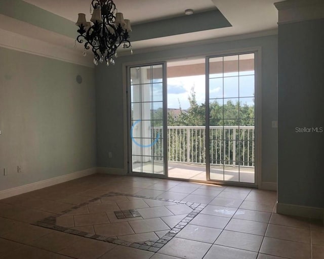 tiled empty room featuring a tray ceiling, ornamental molding, and an inviting chandelier