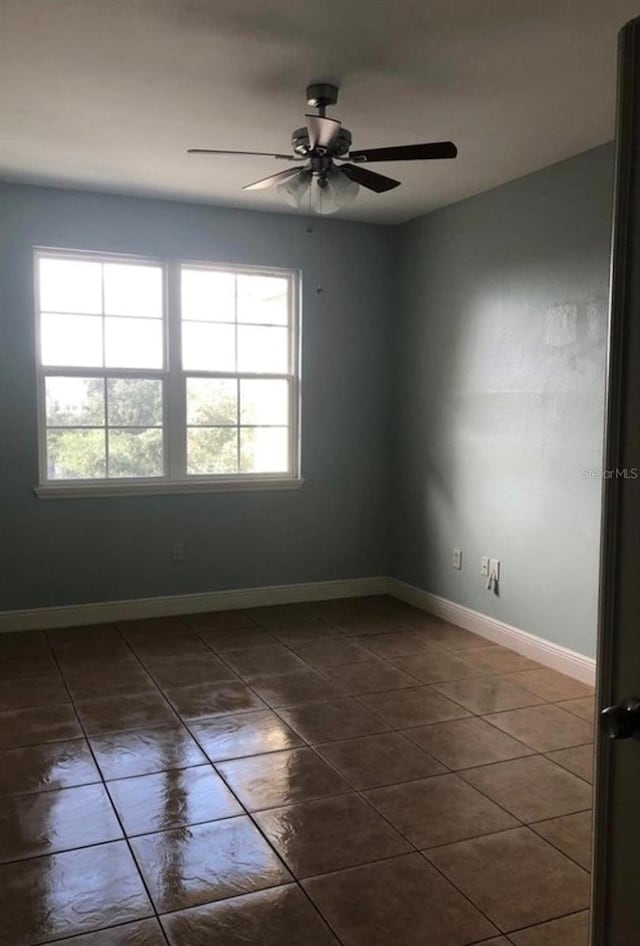 empty room with ceiling fan, plenty of natural light, and dark tile patterned floors