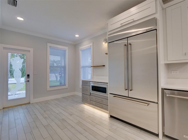 kitchen featuring white cabinets, built in appliances, and crown molding