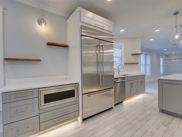 kitchen featuring crown molding, sink, built in appliances, decorative light fixtures, and gray cabinets