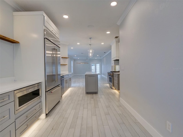 kitchen featuring light wood-type flooring, ornamental molding, built in appliances, gray cabinets, and hanging light fixtures