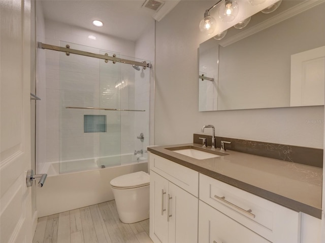 full bathroom with vanity, bath / shower combo with glass door, crown molding, hardwood / wood-style flooring, and toilet