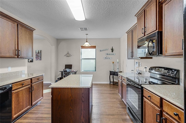 kitchen featuring black appliances, hanging light fixtures, a center island, and hardwood / wood-style floors