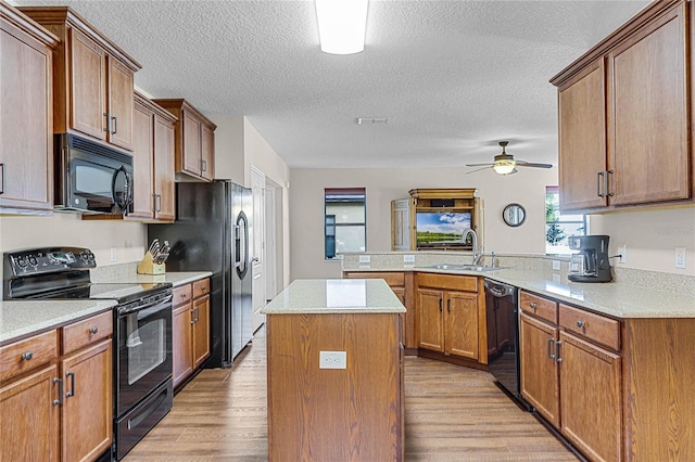 kitchen with kitchen peninsula, black appliances, a kitchen island, ceiling fan, and sink