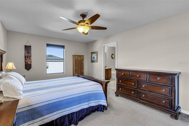 bedroom with ceiling fan, light colored carpet, connected bathroom, and a textured ceiling