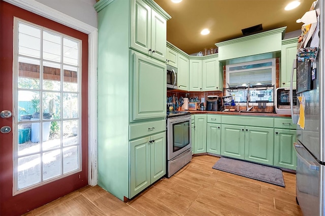 kitchen featuring sink, green cabinetry, tasteful backsplash, light hardwood / wood-style floors, and stainless steel appliances