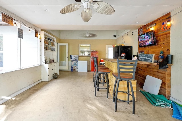 bar with refrigerator, wood walls, ceiling fan, and concrete floors