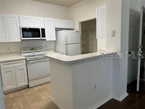 kitchen featuring white fridge, range, kitchen peninsula, and white cabinetry