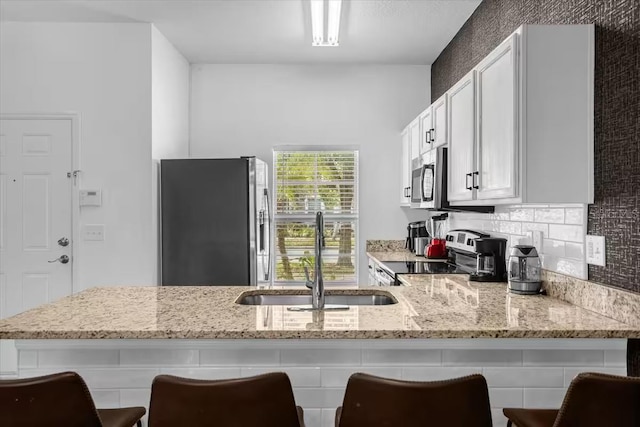 kitchen with a breakfast bar, sink, light stone counters, and stainless steel appliances