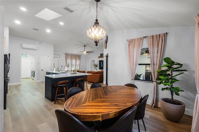 dining area featuring ceiling fan with notable chandelier, a wall mounted AC, sink, light hardwood / wood-style flooring, and washer / dryer