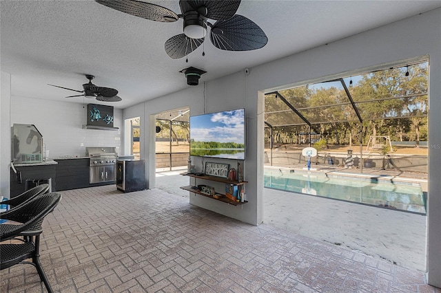 view of patio with an outdoor kitchen, ceiling fan, grilling area, and glass enclosure