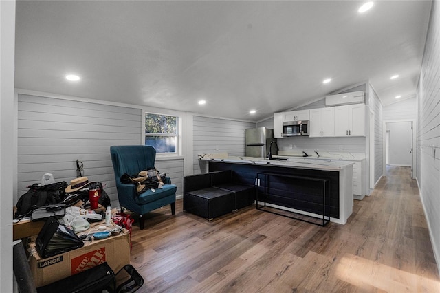 kitchen with kitchen peninsula, appliances with stainless steel finishes, light hardwood / wood-style floors, white cabinetry, and lofted ceiling