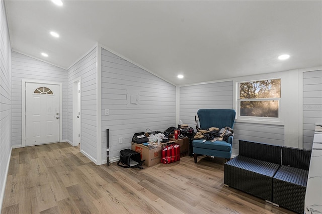 living area with wooden walls, light hardwood / wood-style flooring, and lofted ceiling