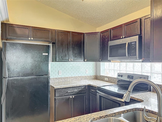 kitchen with lofted ceiling, a textured ceiling, appliances with stainless steel finishes, light stone countertops, and decorative backsplash