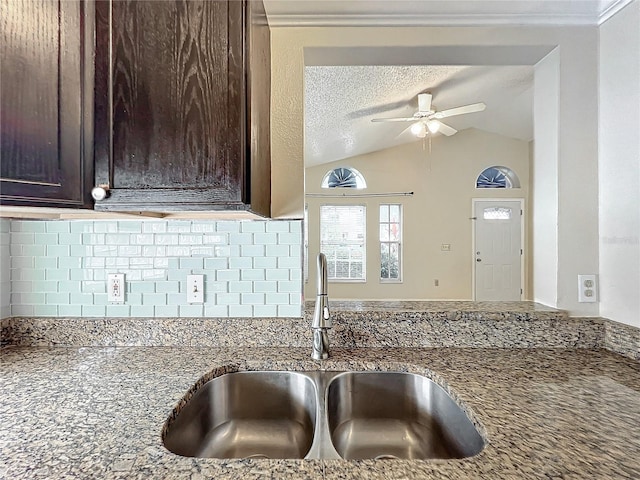 kitchen featuring stone counters, vaulted ceiling, sink, decorative backsplash, and a textured ceiling