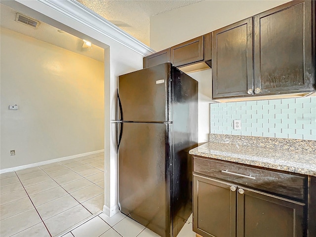 kitchen featuring light tile patterned floors, light stone counters, a textured ceiling, black fridge, and decorative backsplash