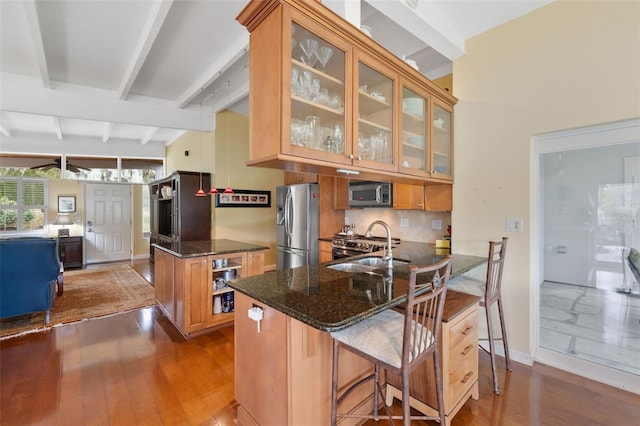 kitchen featuring a breakfast bar, dark stone counters, beam ceiling, kitchen peninsula, and stainless steel appliances