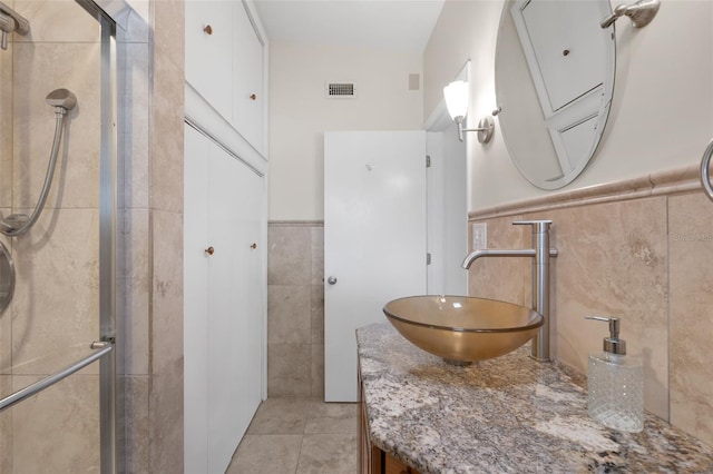 bathroom featuring vanity, tile patterned floors, tile walls, and a shower with shower door