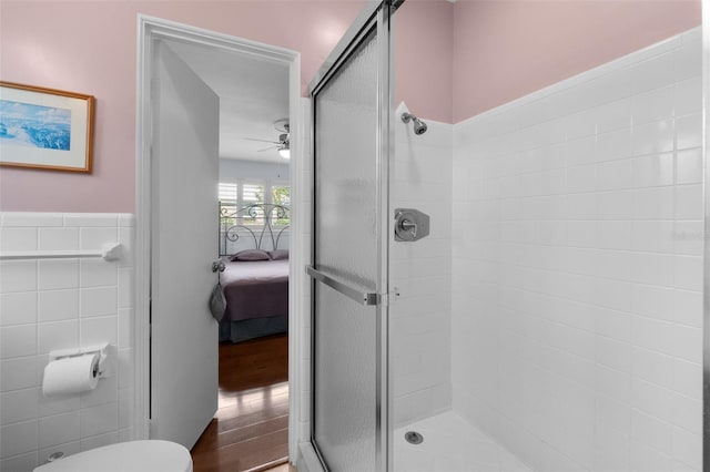 bathroom with ceiling fan, a shower with shower door, tile walls, and toilet