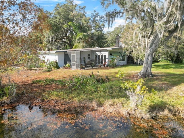 rear view of property featuring a lawn, a sunroom, and a water view