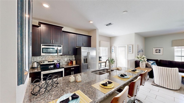 kitchen featuring sink, dark stone countertops, tasteful backsplash, dark brown cabinets, and stainless steel appliances