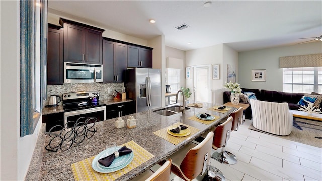 kitchen featuring sink, decorative backsplash, appliances with stainless steel finishes, stone countertops, and dark brown cabinets