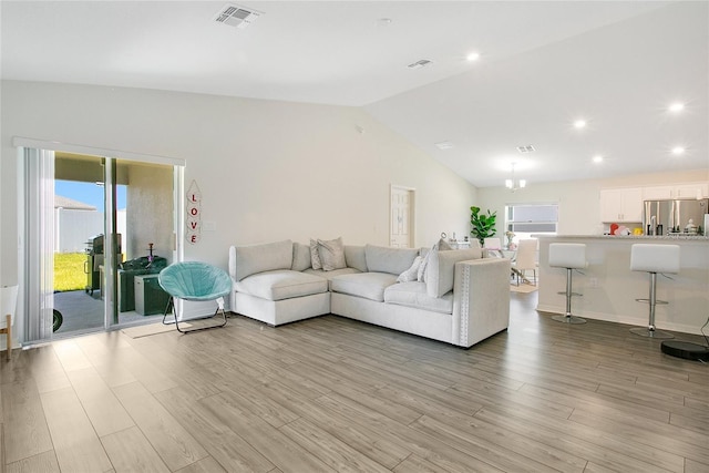 living room with plenty of natural light, an inviting chandelier, light wood-type flooring, and vaulted ceiling