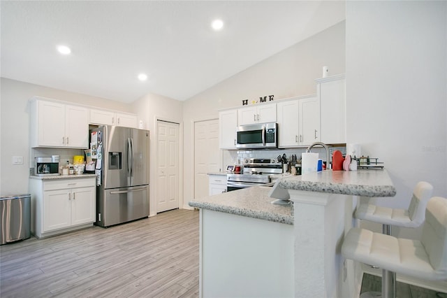 kitchen with kitchen peninsula, appliances with stainless steel finishes, backsplash, a breakfast bar, and white cabinetry