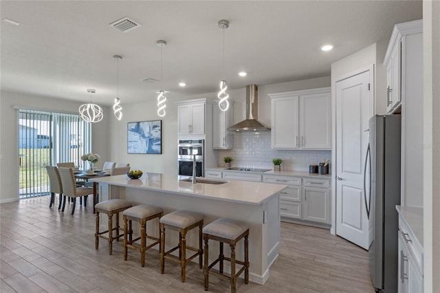 kitchen with white cabinetry, light countertops, wall chimney range hood, appliances with stainless steel finishes, and pendant lighting