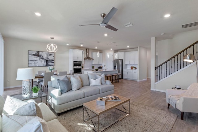 living room featuring ceiling fan, light wood finished floors, stairway, and recessed lighting