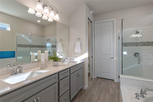 bathroom featuring a stall shower, wood finished floors, a sink, and double vanity