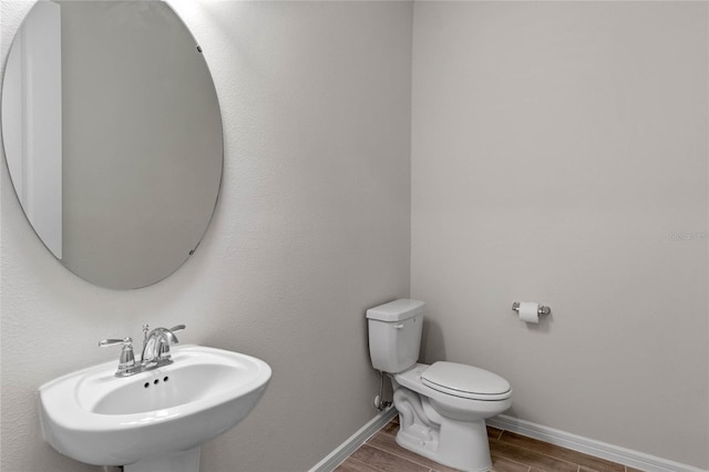 half bathroom featuring toilet, wood tiled floor, baseboards, and a sink