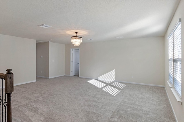 empty room featuring light carpet, a textured ceiling, baseboards, and an inviting chandelier