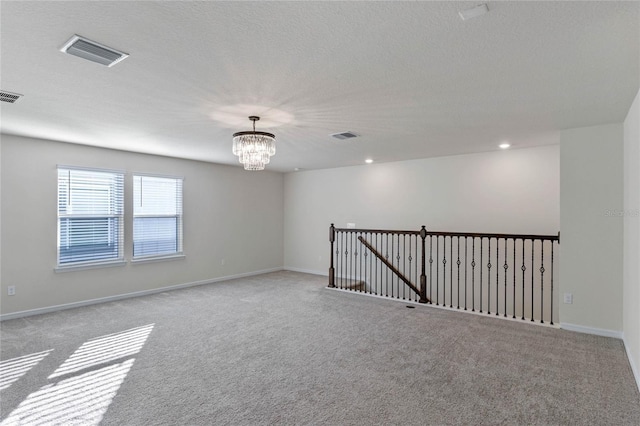 spare room featuring light colored carpet, visible vents, and a notable chandelier