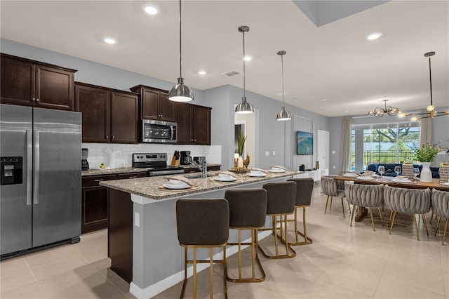 kitchen with a kitchen island with sink, hanging light fixtures, light stone countertops, appliances with stainless steel finishes, and a chandelier