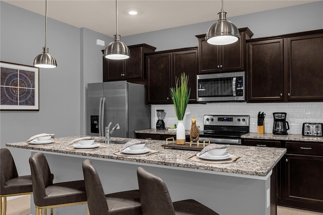 kitchen featuring a center island with sink, stainless steel appliances, hanging light fixtures, and a breakfast bar area