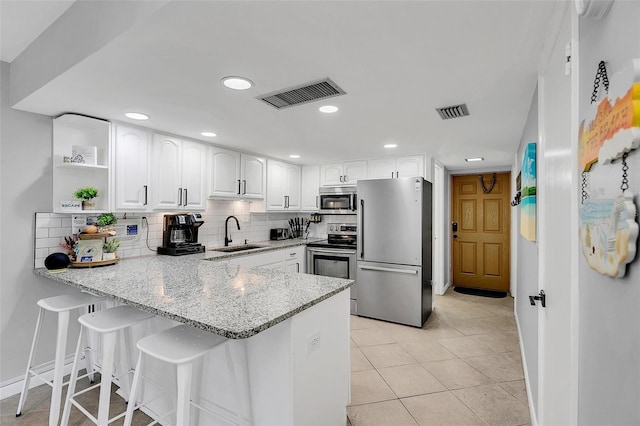 kitchen featuring white cabinetry, sink, stainless steel appliances, light stone counters, and kitchen peninsula