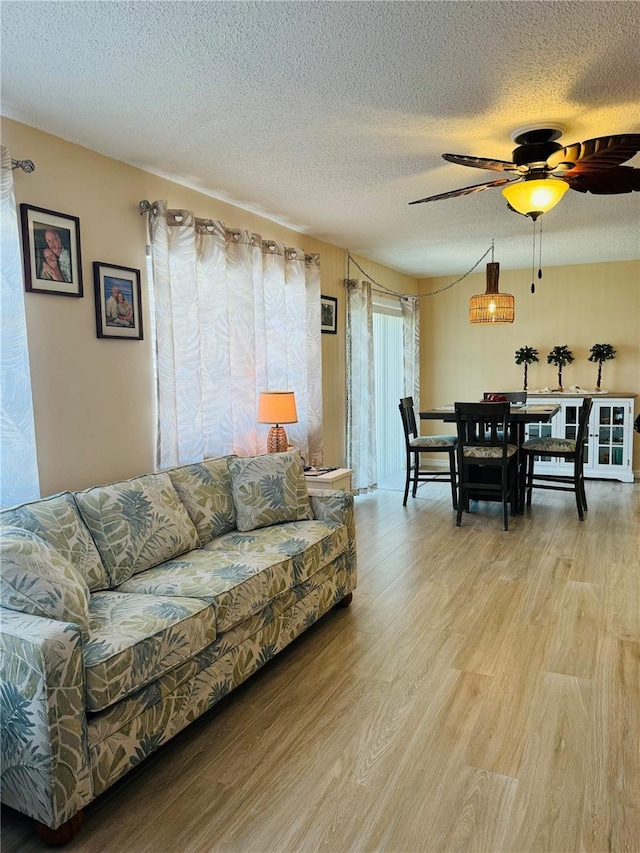 living room with ceiling fan, a textured ceiling, and light wood-type flooring