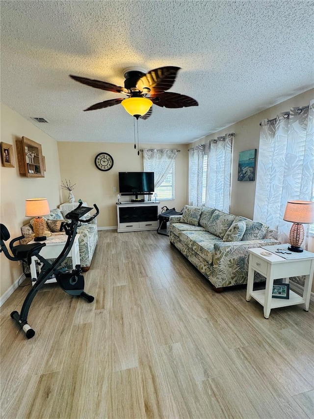 living room featuring ceiling fan, a textured ceiling, and light wood-type flooring