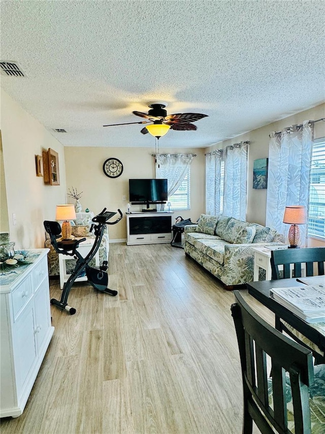 living room featuring ceiling fan, a textured ceiling, and light hardwood / wood-style floors