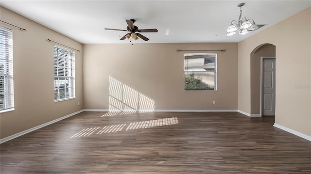 empty room with arched walkways, dark wood-style floors, ceiling fan with notable chandelier, and baseboards