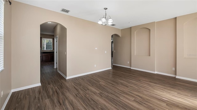 unfurnished room with arched walkways, visible vents, dark wood-type flooring, and baseboards