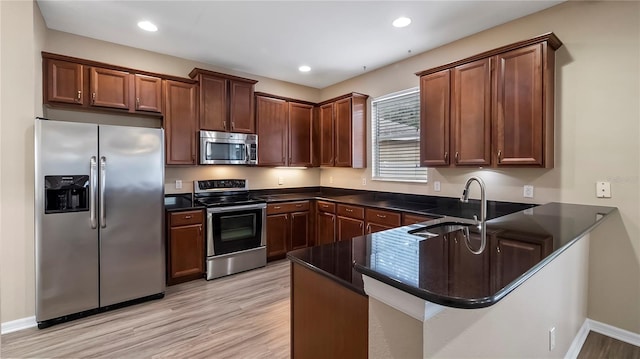 kitchen featuring a peninsula, recessed lighting, a sink, light wood-style floors, and appliances with stainless steel finishes