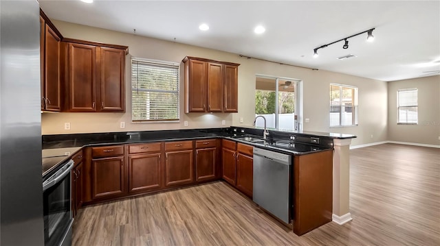 kitchen featuring light wood-style flooring, a sink, open floor plan, appliances with stainless steel finishes, and a peninsula