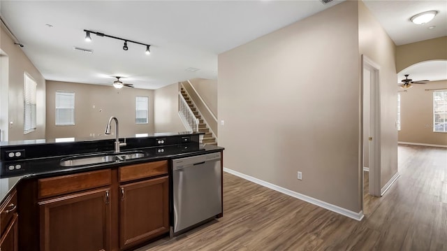 kitchen featuring stainless steel dishwasher, dark countertops, light wood-style flooring, and a sink