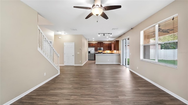 unfurnished living room with dark wood-type flooring, a ceiling fan, and baseboards