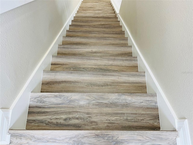 staircase featuring wood finished floors and a textured wall