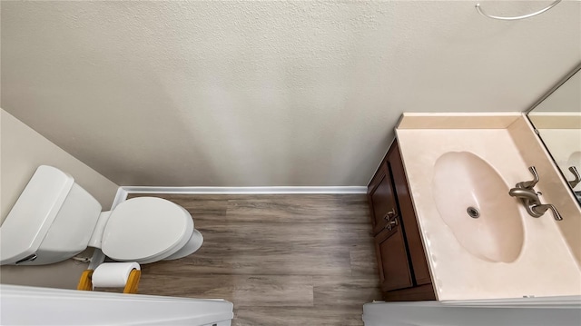 half bath with a textured ceiling, toilet, vanity, and baseboards